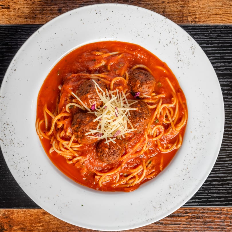 Pastaloni's spaghetti and meatballs with rich red sauce, topped with shredded cheese, on a white plate.