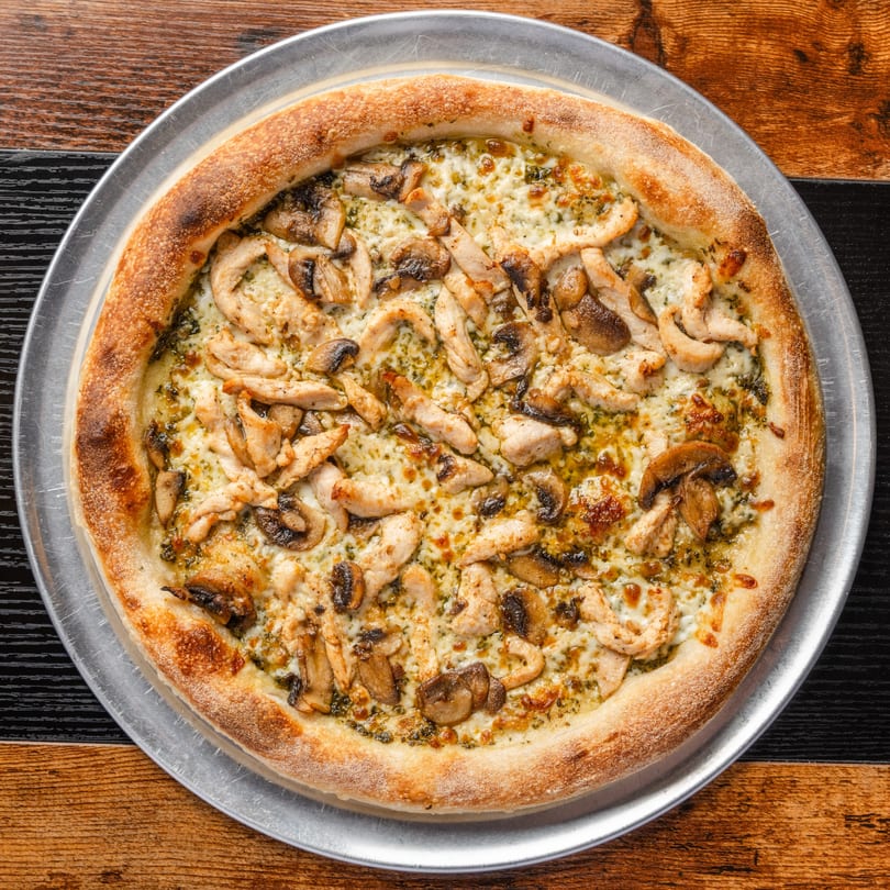 Pastaloni's chicken and mushroom pizza with pesto and cheese on a metal tray.