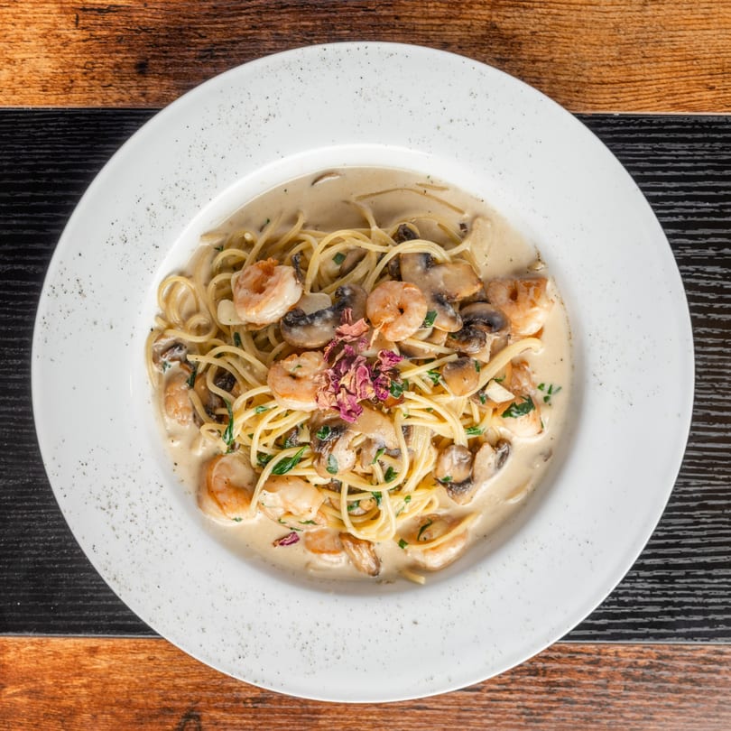 Pastaloni's creamy spaghetti with shrimp, mushrooms, and herbs, garnished with dried rose petals.