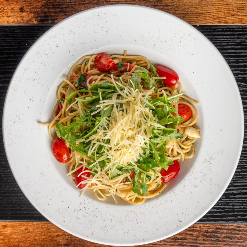 Pastaloni's spaghetti with cherry tomatoes, arugula, and grated Parmesan cheese in a white bowl.