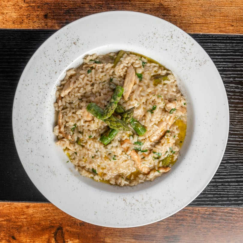 Creamy chicken and asparagus risotto, garnished with fresh herbs, served on a white plate.