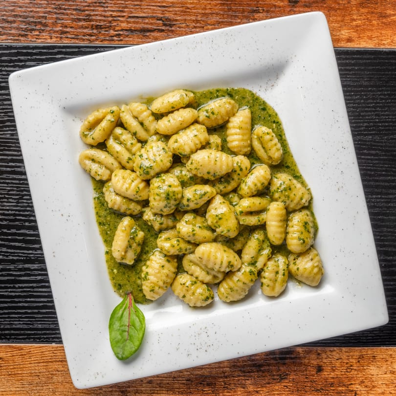 Pastaloni's gnocchi with vibrant green pesto sauce and a fresh garnish on a white plate.