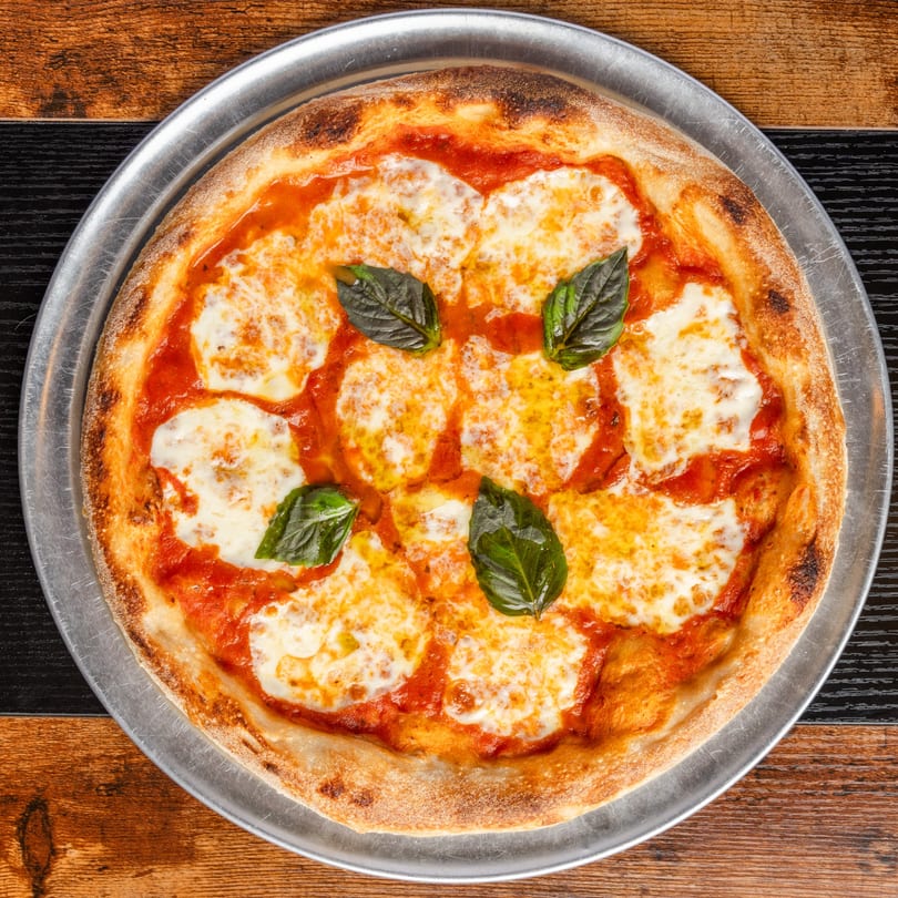 A Pastaloni Margherita pizza with melted mozzarella, red sauce, and fresh basil on a metal tray.